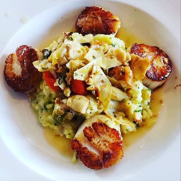 Seared scallops surrounding a bed of risotto with artichoke hearts and cherry tomatoes.