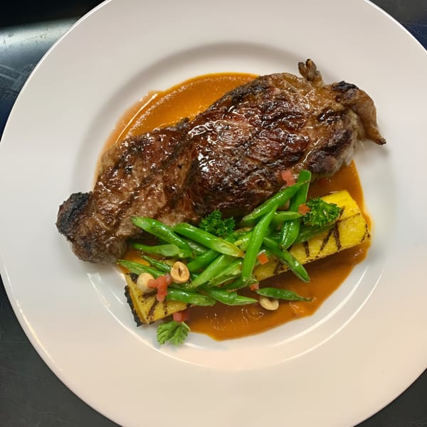 Grilled steak with green beans, polenta, and a rich sauce on a white plate.