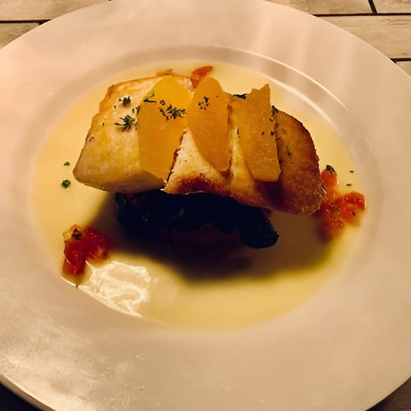 Italian dish with toasted bread, orange slices, and herbs in a shallow broth on a white plate.