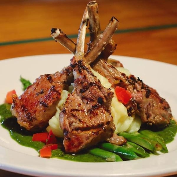 Grilled lamb chops with mashed potatoes, green beans, and red bell peppers on a white plate.